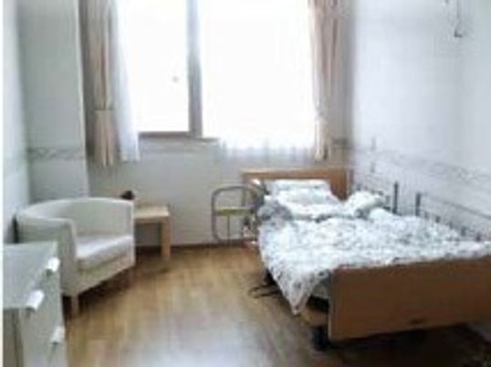 寝具付きのベッドやいすが置かれたフローリングの居室には大きな窓が付き明るい雰囲気。