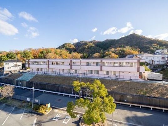 2階建ての建物は白を基調としていて、横に長い。周辺には山や自然があり、駐車場もある。