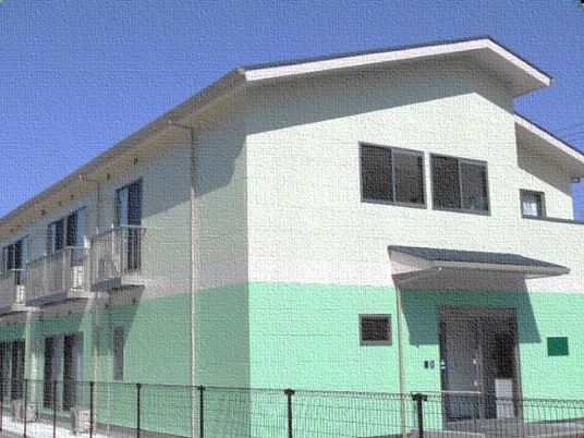 ２階建ての建物は上半分が白、下半分がグリーンの２色使い。玄関部分には屋根が付いている。
