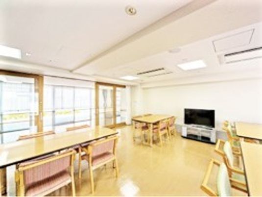 大きなテレビが設置された共有スペースには、木製のダイニングテーブルが複数置かれている。