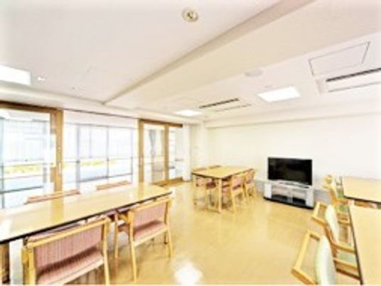 大きなテレビが設置された共有スペースには、木製のダイニングテーブルが複数置かれている。