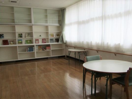 壁一面が本棚となっている共有スペースは窓も大きく明るい。丸いテーブルには椅子が置かれている。