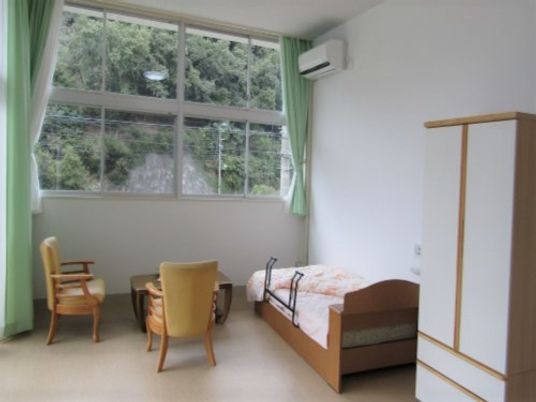 居室にはベッドやクローゼット、いすセットなどがありくつろげるスペースとなっている。窓の外には自然が広がっている。