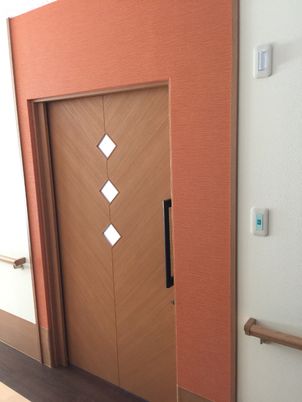 居室のドアはブラウン系の引き戸。ダイヤモンド型の模様が3つ付いている。ドアのすぐそばまで手すりが設置されている。