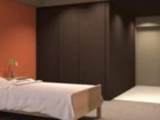 寝具付きのベッドやクローゼットが置かれた部屋にはオレンジ系のアクセントクロスが貼られている。