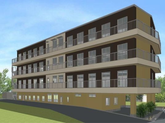 ブラウン系の４階建ての建物は落ち着いた雰囲気。建物の周辺には緑も見える。