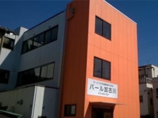 グレーとオレンジの3階建ての建物。玄関の上には施設名が大きく書かれている。