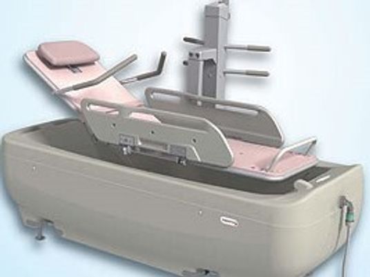 寝たまま入浴できる寝台浴が設置されている。ピンクとグレーの色合い。