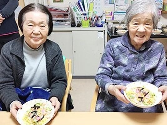 ちらし寿司が盛られた皿を両手で持って微笑んでいる２名の高齢女性たち。