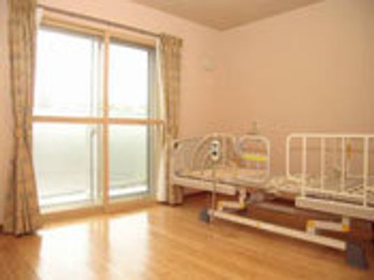 手すり付きのベッドが置かれた居室。窓が大きく明るい雰囲気。
