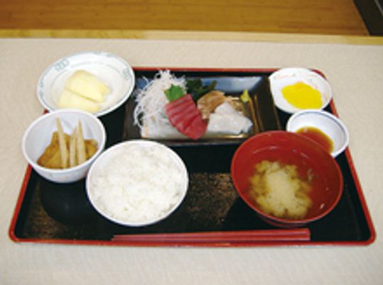 黒いトレーに並べられた和風の食事。刺身や野菜の小鉢などがおかずとしてある。