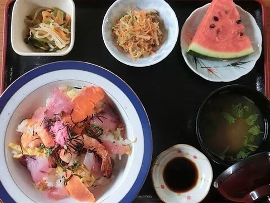 具沢山の海鮮丼にスイカのスライス、野菜の和え物、みそ汁などが並んでいる。