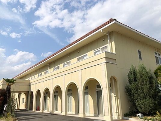 ベージュの２階建ての建物は日当たりがいい場所に建っていて、窓もたくさんついている。