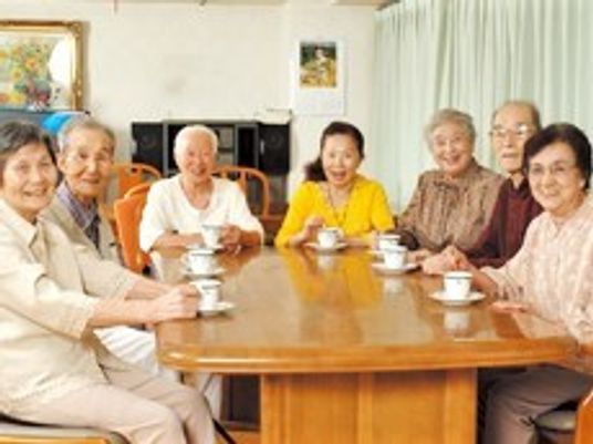 男女の入居者が木製のテーブルを囲んで笑顔でティータイムを過ごしている様子。