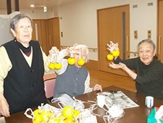 施設内のリビングで何かを掲げて笑顔で写真に納まる高齢者の様子