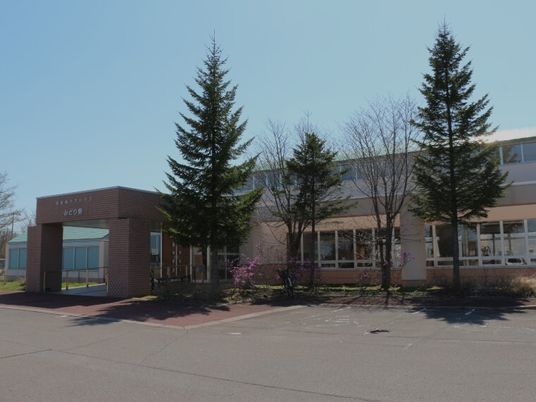 広い敷地内には駐車場があり、ブラウン系の建物には車寄せがあり、木もたくさん植えられている。