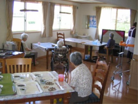明るい日差しが差し込む食堂。数名の入居者がいくつかのテーブルに分かれて座っている。