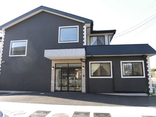 2階建ての建物はダークカラーでまとめられ、玄関には屋根と自動ドアが付き、段差も解消されている。