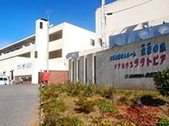 ラクトピアの看板がある壁とその奥にある建物の写真。手前に中庭がある様子