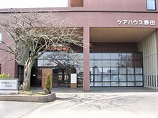 ブラウン系の建物は5階建てで重厚感があり、建物の前には大きな木や花が植えられている。