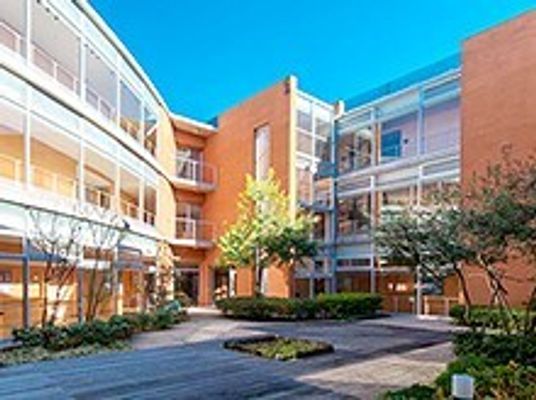 大きな明るいブラウン系の建物がある敷地内には、気がたくさん植えられた庭もある。