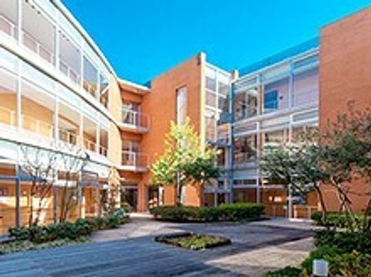 大きな明るいブラウン系の建物がある敷地内には、気がたくさん植えられた庭もある。