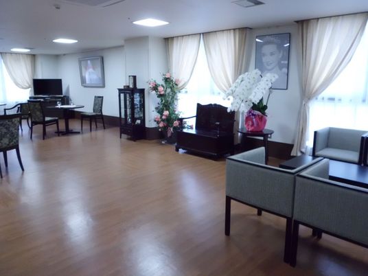 屋外で笑顔で過ごしている車いすの高齢女性と付き添いのエプロンを付けた若い女性スタッフ。
