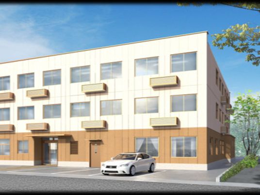 白とブラウンの3階建ての建物は日当たりのいい場所に建っていて、建物の前には駐車場がある。