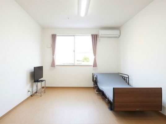 一人用のベッドとエアコンが置いてある施設内の居室。左側にテレビが置いてある様子