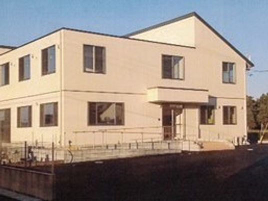 2階建ての建物は落ち着いたベージュ系で庭園や駐車スペースもある。