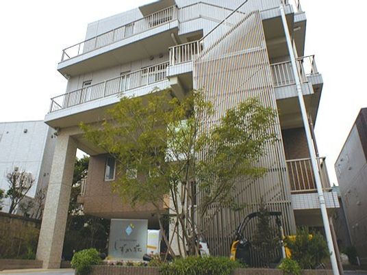 白を基調とした4階建ての建物の前には館銘板が設置されていて、草木が植えられている。