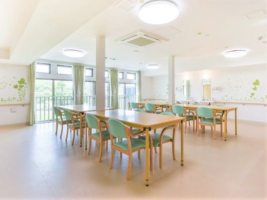 木のテーブルと椅子が整然と並んでいる施設内の一室。窓の向こうに景色が見えている