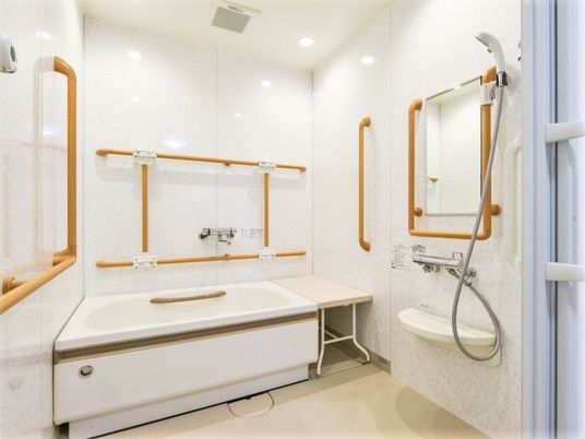 四方の壁に満遍なく手すりが取り付けられている浴室の様子。座った姿勢で入浴できる腰掛もある