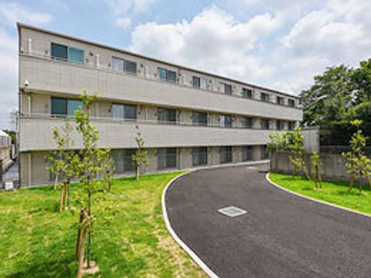 鉄骨造３階建ての建物を中庭から写した写真。散歩できる遊歩道が整備されている様子