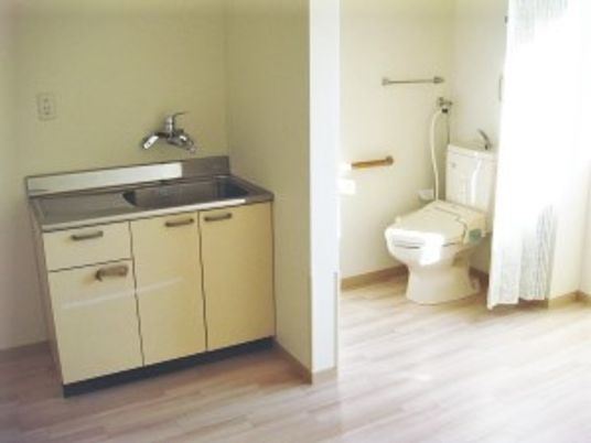 居室内のキッチンとドアレスのトイレを写した写真。広めのワンルームの部屋の様子