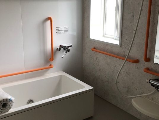 オレンジの手すりがたくさん付いた浴室には一人用の浴槽が設置され、シャワーもある。