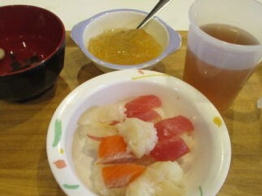 鮭やマグロ、貝などの一口サイズの寿司が盛られた皿を囲むようにお茶やゼリー、汁物もある。
