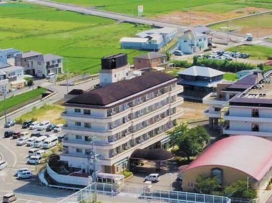 ブラウンの屋根が付いた5階建ての建物のそばには体育館のような建物屋3階建ての建物もあり、周辺には田畑も広がっている。
