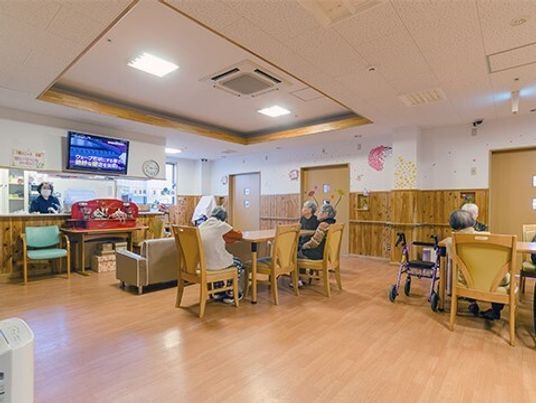 ダイニングテーブルが2組あり、それぞれに入居者がいて、対面式のキッチンにはスタッフがいる。