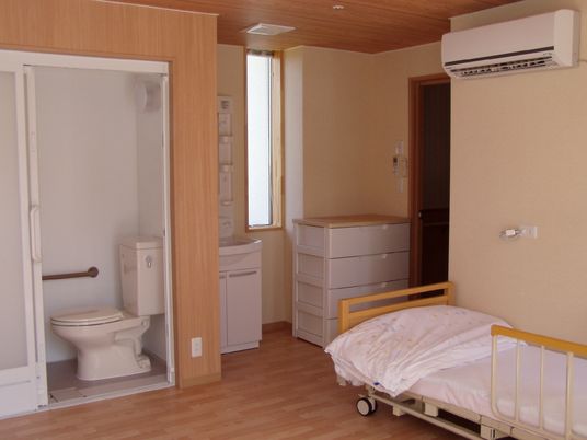 寝具付きのベッドやエアコン、トイレなどがそろったフローリングの部屋。緊急通報装置付き。