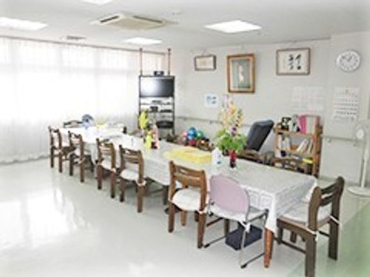 テーブルクロスがかけられた長いテーブルが中央に置かれ、テレビや観葉植物も置かれている。