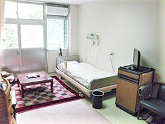 ベッドやテーブル、テレビや冷蔵庫などがそろった明るい居室。