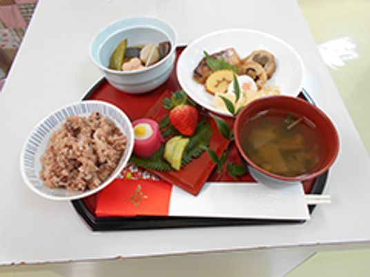 黒い盆の上には寿の文字が書かれた箸や赤飯、煮物などが並んでいる。