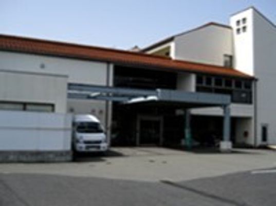 白を基調とした大きな建物の屋根は赤で日当たりのいい場所に建っている。敷地内には駐車場もあり、車も止まっている。