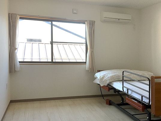 窓が付いたフローリングの居室には寝具付きのベッド屋エアコン、カーテンがあり、家具などは持ち込まれていない。
