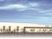 ベージュの外壁の建物は日当たりのいい場所にあり、駐車場もある。数名の人が玄関の周りにいある。