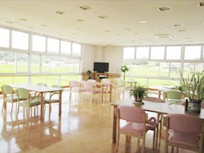 壁一面が窓となっている明るいリビングダイニングにはテーブルセットが複数とテレビがある。