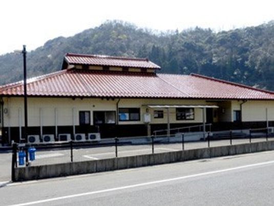 広い敷地内には駐車スペースが確保され、平屋建ての建物の後ろには山々が連なっている。
