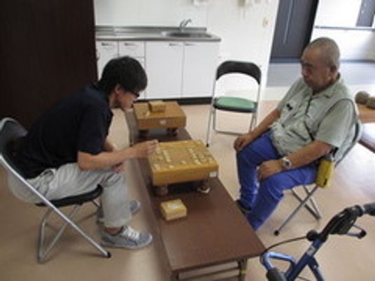 スタッフと将棋を楽しんでいる様子の高齢者。施設内の娯楽の様子
