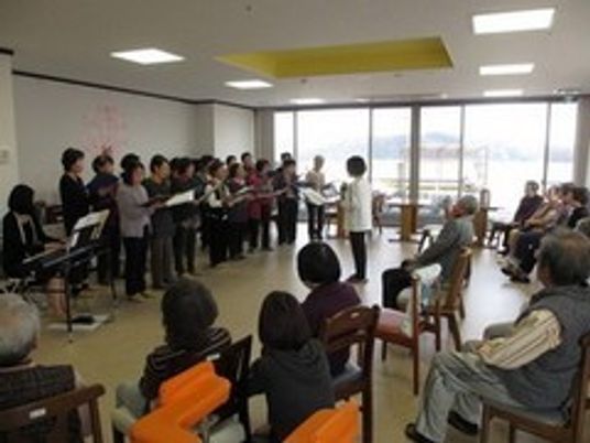 高齢者向け施設内でボランティアの人が催し物を開催している様子。施設内スタッフ、手前に高齢者が並んでいる